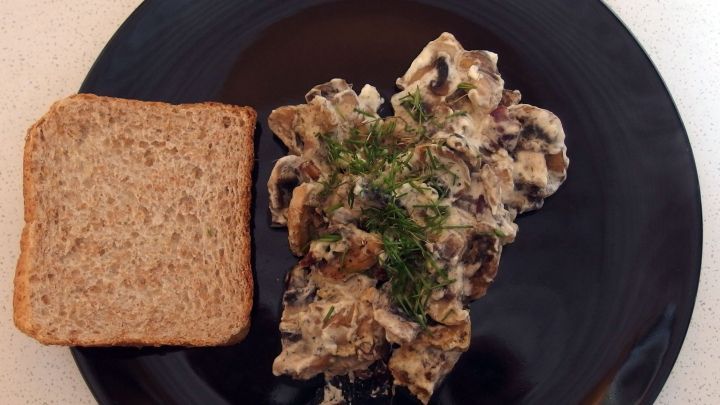 Eine cremige Pilzpfanne wird auf einem schwarzen Teller serviert, neben einer Scheibe Vollkornbrot.