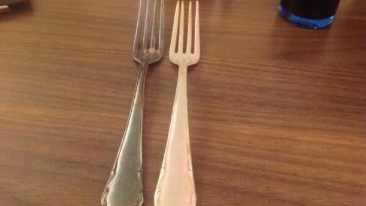 Ein silberner und ein Messinggabel liegen nebeneinander auf einem Holztisch, der einen Kontrast zwischen Silberbesteck zeigt.