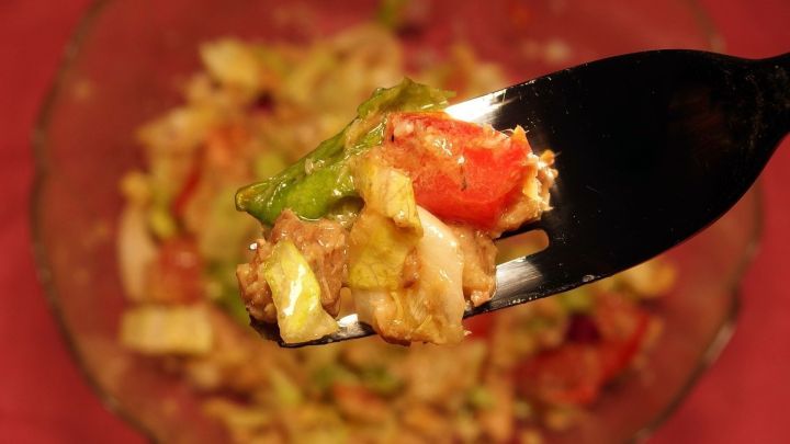 Ein L&ouml;ffel Sardinensalat wird hochgehoben, um die frischen Zutaten im Hintergrund zu zeigen.