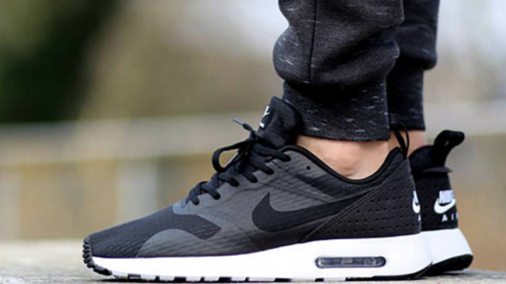 Schwarze Turnschuhe stehen auf einem Steinsockel. Eine Person tr&auml;gt sie, w&auml;hrend sie drau&szlig;en in der Natur steht.