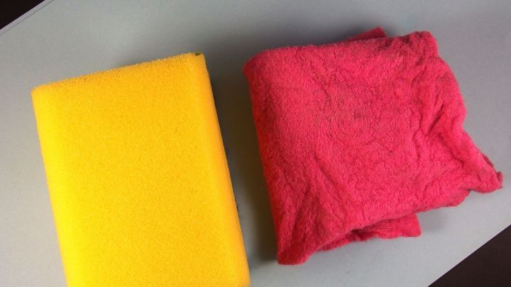 Ein gelber Schwamm und ein rosa Sp&uuml;llappen liegen auf einer grauen Fl&auml;che, bereit zur Reinigung in der Mikrowelle.