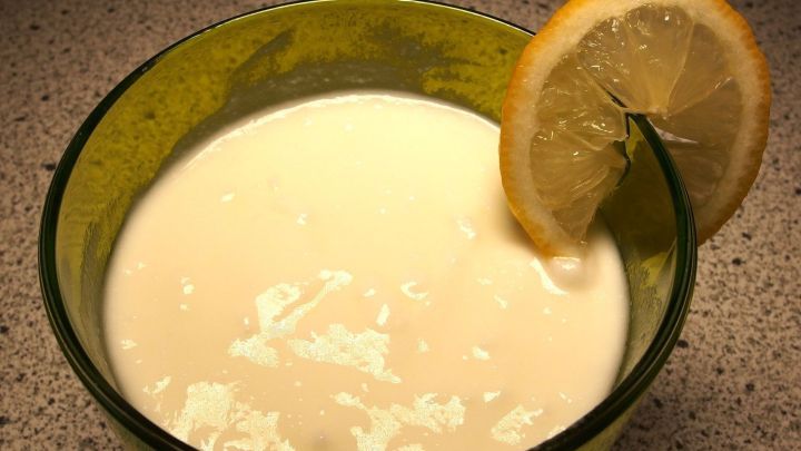 Eine gr&uuml;ne Sch&uuml;ssel enth&auml;lt einen kalten, cremigen Nachtisch mit einer Zitronenscheibe am Rand, alles auf einer neutralen Fl&auml;che.