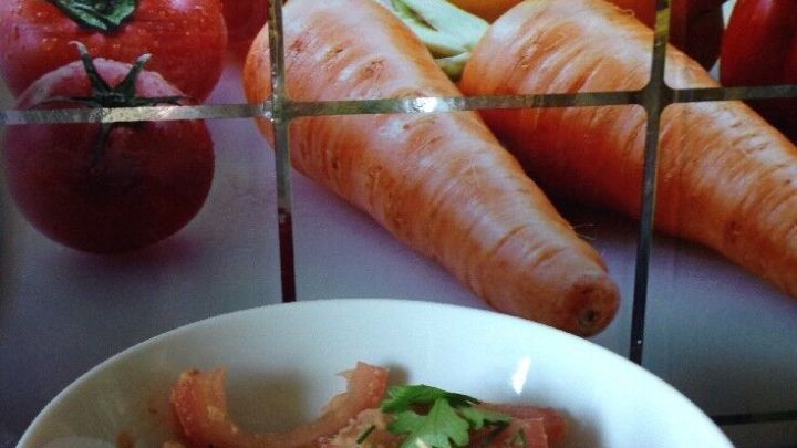 Ein frischer Tomatensalat in einer wei&szlig;en Sch&uuml;ssel, umgeben von einer bunten Gem&uuml;seanzeige mit Karotten und Paprika.