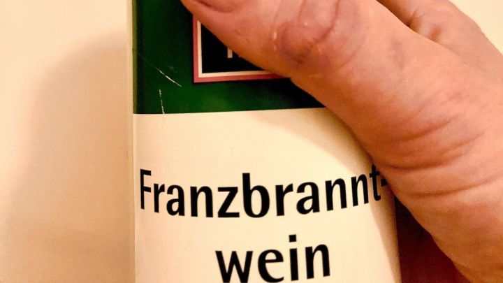 Eine Hand h&auml;lt eine Flasche mit Franzbranntwein, bereit zur Anwendung gegen Schuppen in einem hellen Hintergrund.