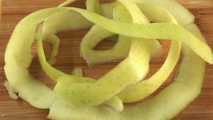 Gr&uuml;ne Apfelschalen liegen spiralf&ouml;rmig auf einem Holzbrett, ideal f&uuml;r die Zubereitung von Apfelschalentee.