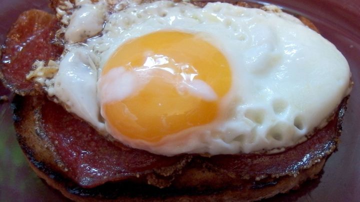 Dunkle Brotscheiben sind mit Salami und einem Spiegelei belegt, angerichtet auf einem braunen Teller.