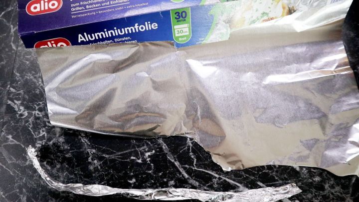 Alu-Papilotten werden vorbereitet, w&auml;hrend eine Rolle Aluminiumfolie auf einer dunklen Oberfl&auml;che sichtbar ist.
