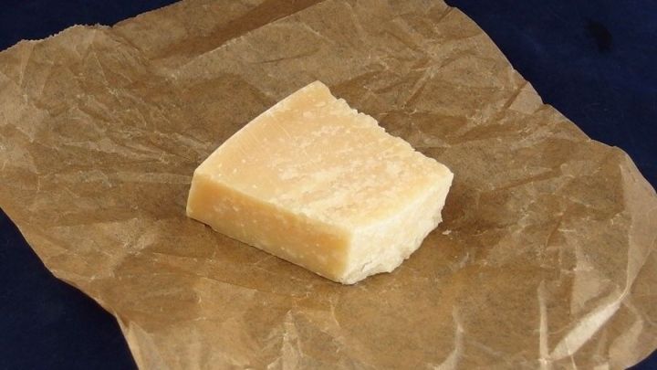 Ein St&uuml;ck K&auml;se liegt auf braunem Backpapier, bereit eingewickelt zu werden, auf einem blauen Untergrund.