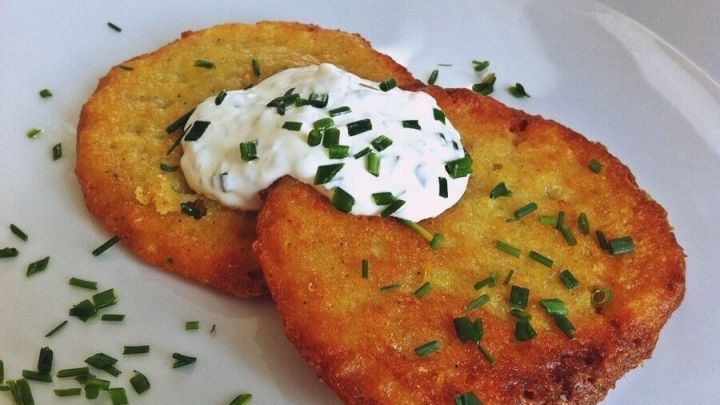 Knusprige Kartoffelr&ouml;sti liegen auf einem Teller, garniert mit einer Portion Sauerrahm und frischem Schnittlauch.