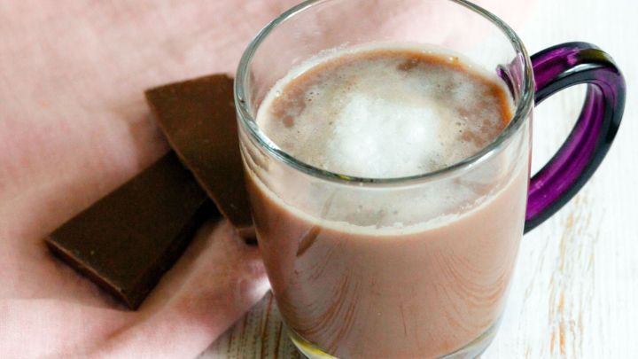 Ein Glas hei&szlig;e Schokolade steht auf einem Tisch, neben einer Schokolade, umgeben von einem rosa Tuch.