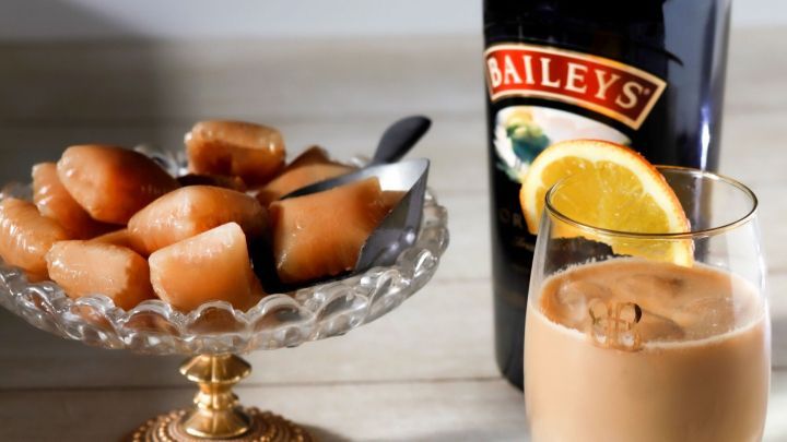 Gefrorene Baileys-W&uuml;rfel liegen auf einem Glasplatten-Teller, w&auml;hrend ein Glas mit Baileys-Cocktail daneben steht.
