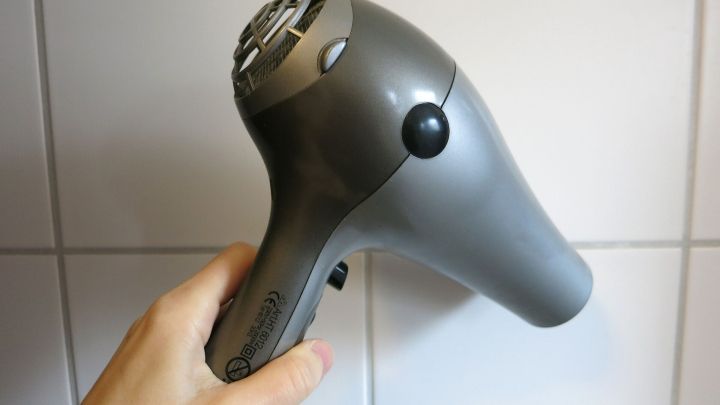 Ein Haartrockner wird von einer Hand gehalten, bereit zur Anwendung in einem Badezimmer mit wei&szlig;en Fliesen.