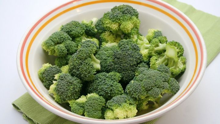 Frischer Brokkoli liegt in einer bunten Sch&uuml;ssel auf einem gr&uuml;nen Tuch, bereit zum Garprozess in der Mikrowelle.