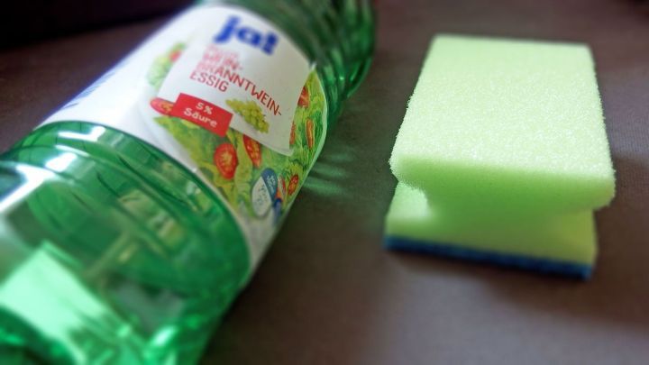 Eine gr&uuml;ne Flasche mit Essig steht neben einem K&uuml;chenschwamm auf einer Tischoberfl&auml;che, bereit zur Reinigung gegen Brechgeruch.