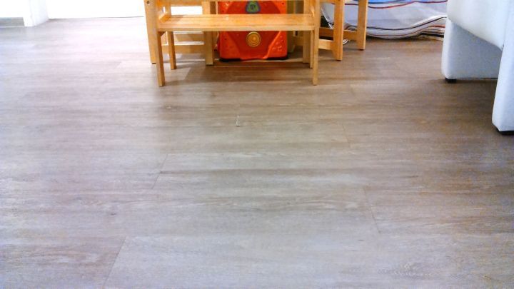 Ein brauner Laminatboden ist zu sehen, auf dem ein kleines Holzregal steht, umgeben von heller Raumgestaltung.