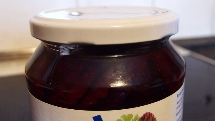 Ein Glas mit einem wei&szlig;en Deckel steht auf einer schwarzen Oberfl&auml;che. Der Inhalt ist dunkelrot und l&auml;sst auf Marmelade schlie&szlig;en.