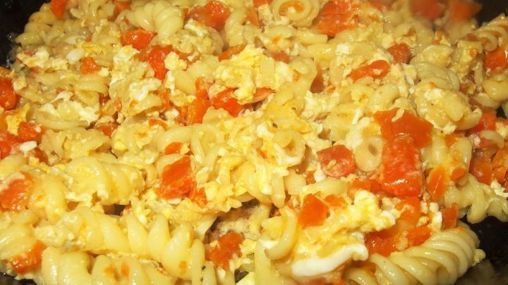 In einer Pfanne werden frische Karottennudeln mit Tomaten und anderen Zutaten gemischt und erhitzt.