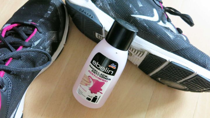 Schwarze Sportschuhe liegen auf einem Boden neben einer Flasche Nagellackentferner, bereit zur Reinigung.
