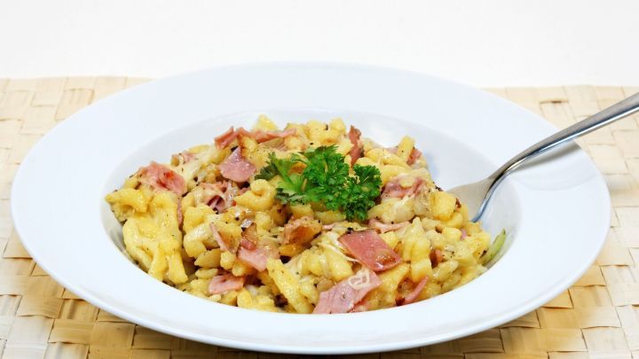 K&auml;sesp&auml;tzle mit Schinken und Petersilie in einer wei&szlig;en Sch&uuml;ssel, auf einem nat&uuml;rlichen Tischuntergrund serviert.