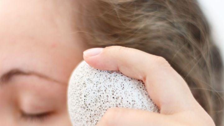 Eine Hand h&auml;lt einen Bimsstein, der sanft auf die Haut eines Gesichts gedr&uuml;ckt wird, um Pickel zu behandeln.