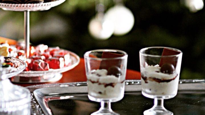 Zwei elegante Gl&auml;ser mit Quark-Schmand-Creme und Sauerkirschen stehen auf einem Serviertablett vor einem festlichen Hintergrund.