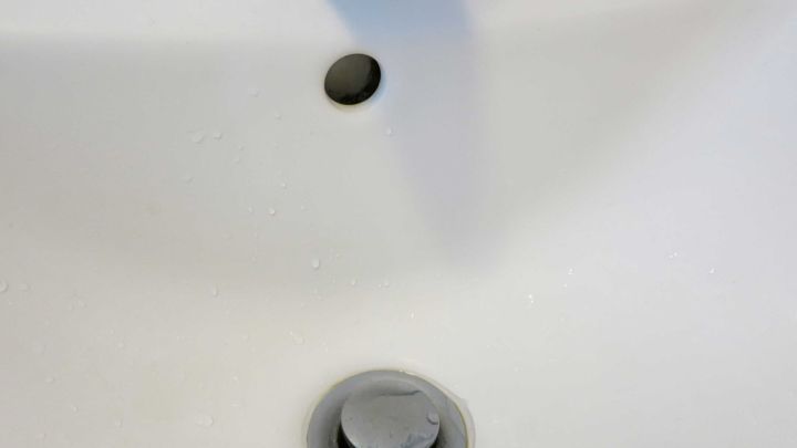 Ein Waschbecken mit einem silbernen &Uuml;berlaufloch, das Kalkschmutz an den R&auml;ndern aufweist, in einem Badezimmer.