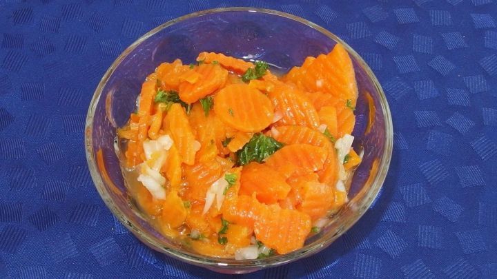 Ein bunter, gekochter Karottensalat in einer Sch&uuml;ssel liegt auf einem blauen Tisch und wartet auf das Servieren.