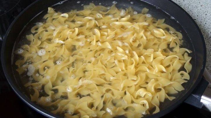 In einer Pfanne kochen Nudeln in sprudelndem Wasser, umgeben von einer modernen K&uuml;chenumgebung.