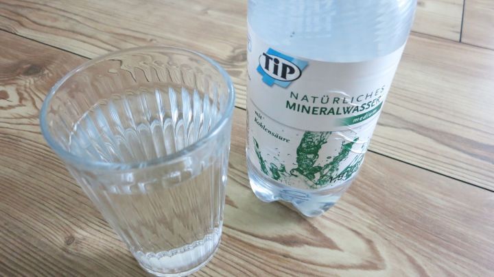 Ein Glas mit kaltem Mineralwasser steht neben einer Flasche auf einem Holzfu&szlig;boden, ideal zur Linderung von Zahnschmerzen.