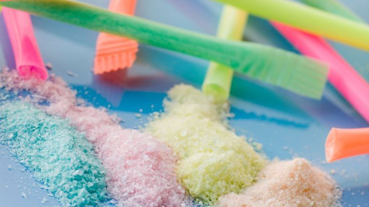 Farbige Zuckerstreifen liegen neben buntem Pulver in verschiedenen Farben auf einer blauen Unterlage, bereit zum Genie&szlig;en.