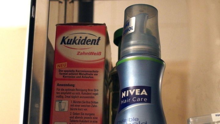 In einem Badezimmerregal stehen eine Packung Kukident und eine Nivea-Spr&uuml;hflasche, die f&uuml;r Zahnpflege und Hautpflege verwendet werden.