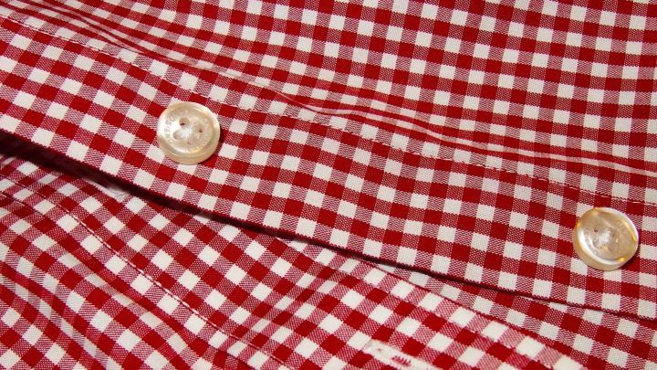 Zwei farblose Kn&ouml;pfe auf einem rot-wei&szlig; karierten Hemd fixieren die Stofflagen, um ein einheitliches Design zu schaffen.