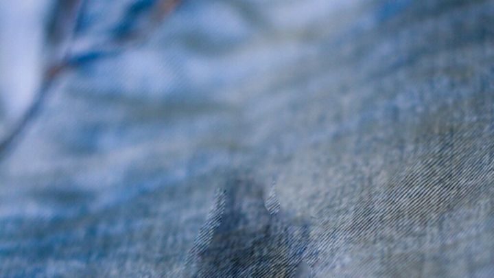 Ein Fettfleck breitet sich auf blauem Stoff aus, vermutlich eine Jeans, und hebt sich dunkel von der Umgebung ab.