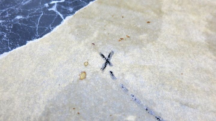 Eine Schatzkarte aus Backpapier zeigt eine schwarze Markierung in Form eines X und eine Linienzeichnung im Hintergrund.