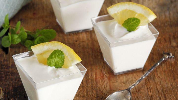 Drei gl&auml;serne Becher mit Joghurtmousse, garniert mit Zitronenscheiben und Minze, stehen auf einem rustikalen Holzuntergrund.
