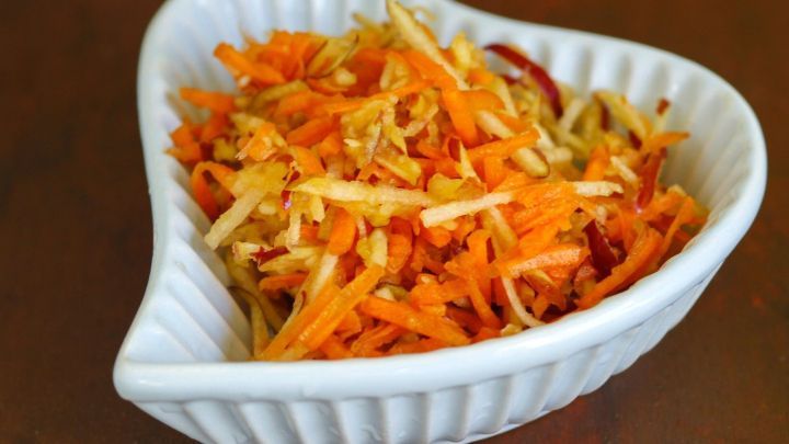 Ein Herzschale enth&auml;lt frisch geriebenen M&ouml;hren-Apfelsalat, appetitlich angerichtet auf einem Holztisch.