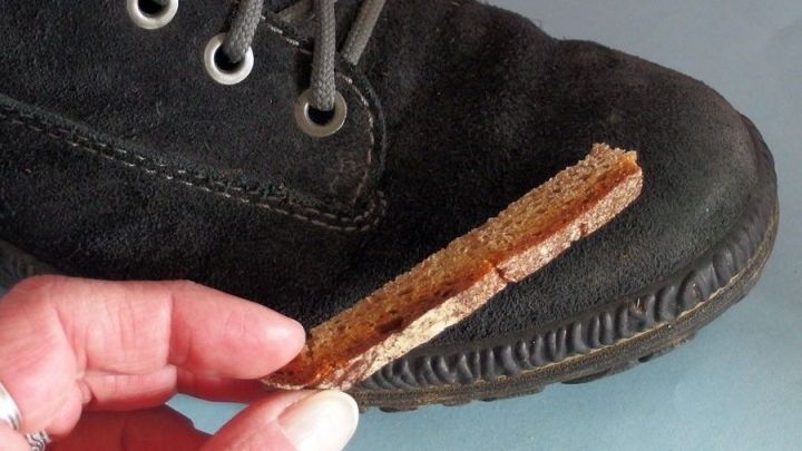 Ein schwarzer Wildlederschuh wird mit einer Brotrinde gereinigt. Die Hand hält die Rinde über die Schuhoberfläche.