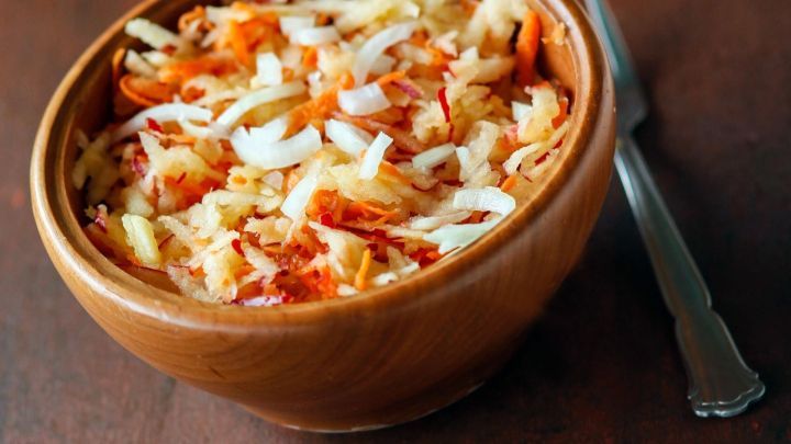 Eine Sch&uuml;ssel mit Karotten-Apfel-Salat steht auf einem Holztisch. Zarte Zutaten sind fein vermischt und gut angerichtet.