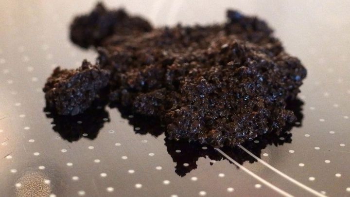 Ein Klumpen Kaffeepr&uuml;tt liegt auf einem schwarzen Glaskeramikfeld, das mit wei&szlig;en Punkten verziert ist.