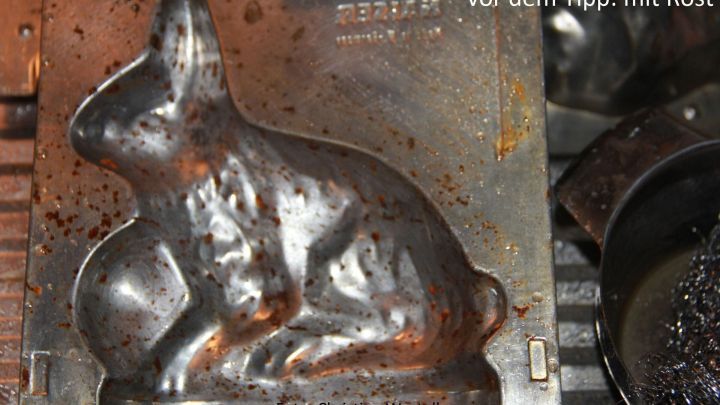 Eine rostige Backform in Form eines Kaninchens, auf der Hinweise zur Entfernung von Rost mit &Ouml;l und Essig zu sehen sind.