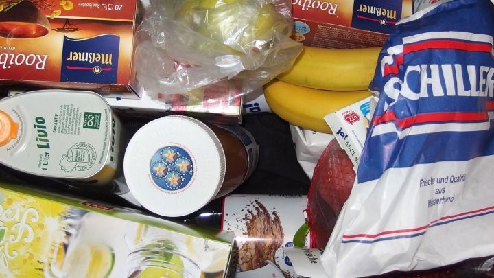 Ein bunter Mix aus Lebensmitteln liegt auf einer Fl&auml;che, darunter Bananen, Getr&auml;nke und Snacks f&uuml;r die Einkaufsliste.
