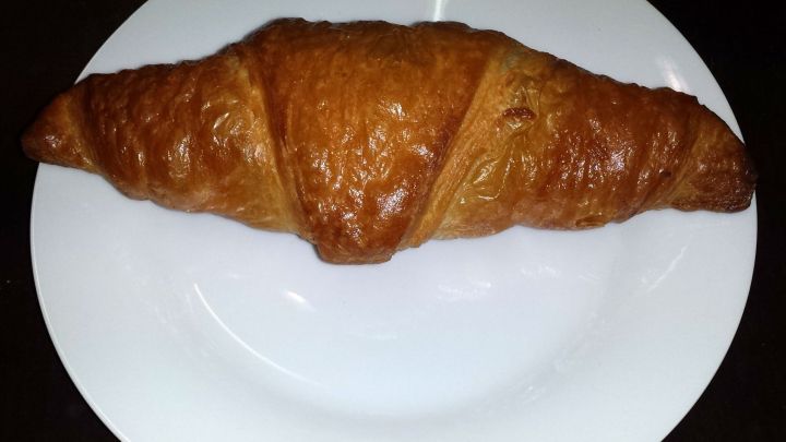 Auf einem wei&szlig;en Teller liegt eine goldbraune, knusprige Bl&auml;tterteigschnecke, die appetitlich aussieht.