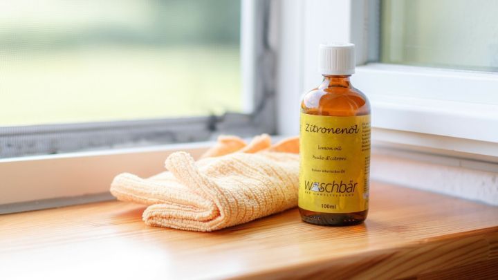 Ein Fl&auml;schchen Zitronen&ouml;l steht auf einer Fensterbank neben einem gelben Tuch, um M&uuml;cken und Insekten fernzuhalten.