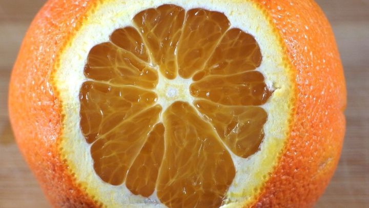 Eine orangefarbene Orange liegt auf einem Holztisch, die Schale ist teilweise entfernt und zeigt die saftigen Segmente.