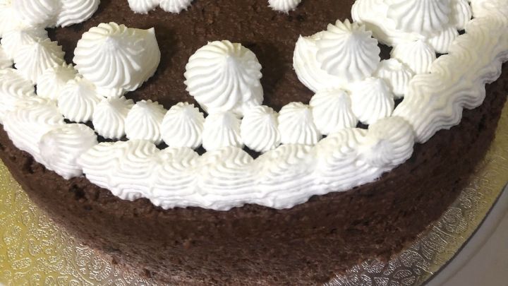 Ein Schokokuchen mit Sahnehaube zeigt die Zahl 51, dekoriert auf einem goldenen Teller in einer hellen K&uuml;che.