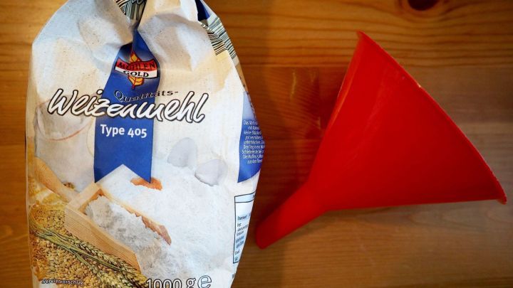 Ein roter Trichter steht neben einer T&uuml;te Weizenmehl, um So&szlig;enklumpen beim Einf&uuml;llen zu verhindern.
