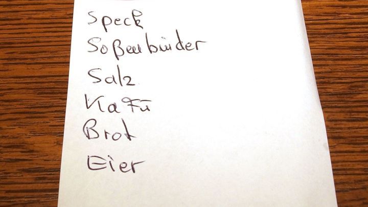 Eine handgeschriebene Einkaufsliste auf einem Notizblatt zeigt verschiedene Lebensmittel wie Speck, Salz und Eier zur Planung von Sparen beim Einkauf.