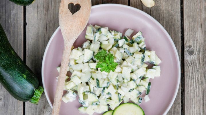 Frischer Zucchinisalat liegt auf einem Teller, umgeben von Zucchini und Zwiebel, bereit zum Servieren.