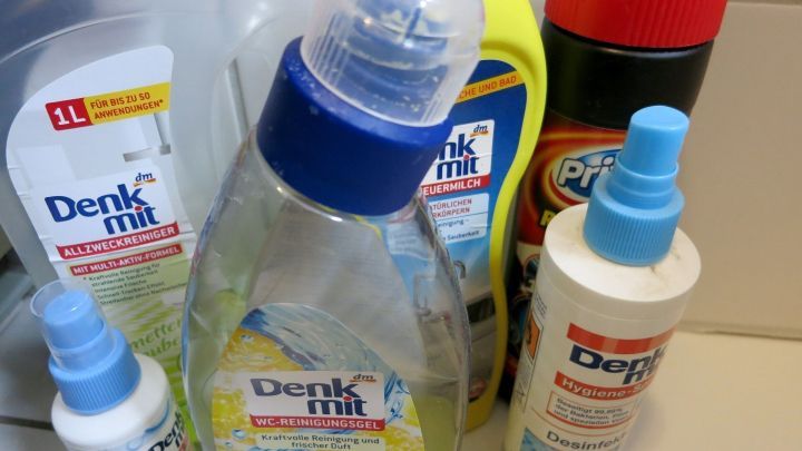 Eine Auswahl an Reinigungsmitteln steht auf einer K&uuml;chearbeitsplatte, darunter Produkte mit der Aufschrift &bdquo;Denk Mit&ldquo;.