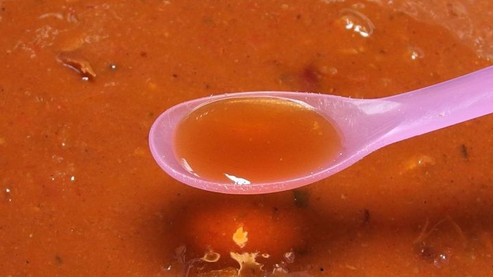 Eine lila L&ouml;ffel voll mit einer salzigen Suppe, die in einem tiefen Teller mit dunkler Br&uuml;he schwimmt.